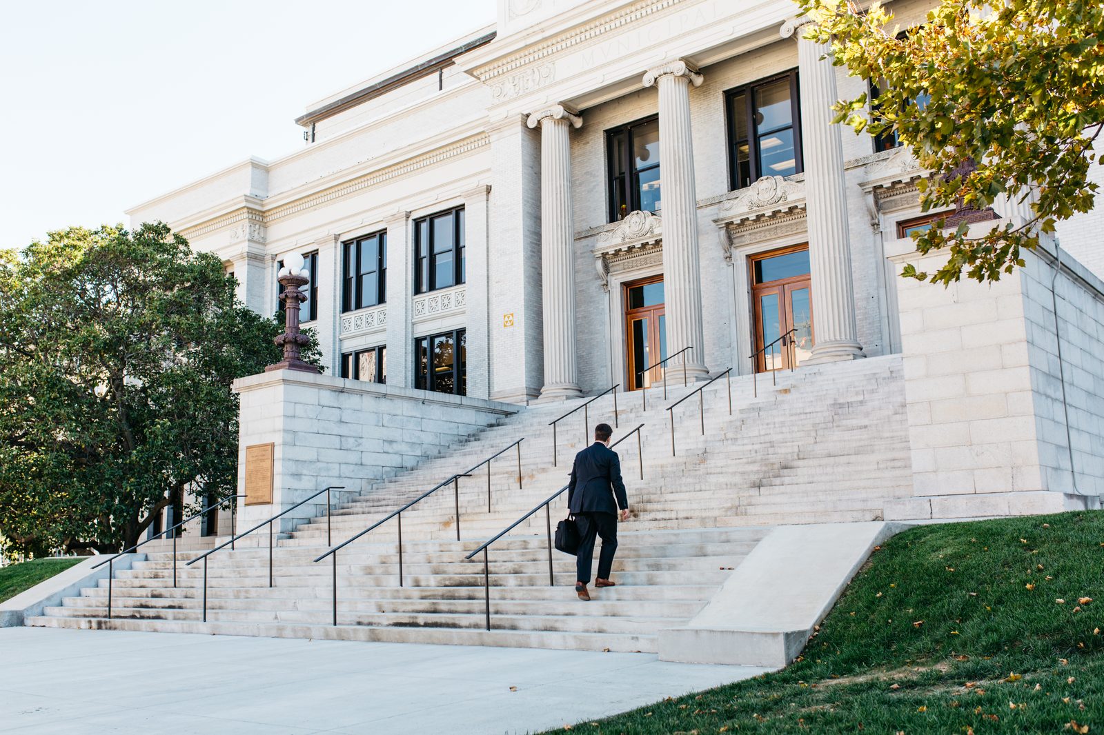 A lawyer with a briefcase climbs the wide stone steps toward a columned courthouse entrance